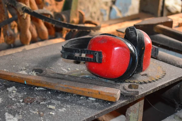 Red noise-protective earphones of wood working carver. Carpenter\'s workshop with slips. Desktop of the joiner. Noise.