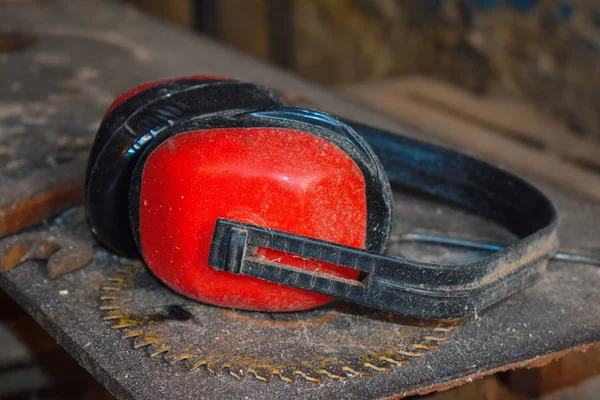 Red noise-protective earphones of wood working carver. Carpenter\'s workshop with slips. Desktop of the joiner. Noise.