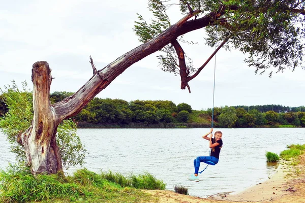 Chica alegre balanceándose en un columpio de cuerda. Tener unas vacaciones de verano divertidas — Foto de Stock