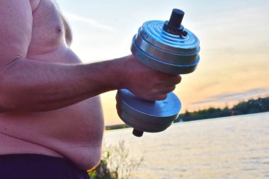 Şişko midesi olan bir adam ağırlık kaldırır. Kilo kaybı parodi