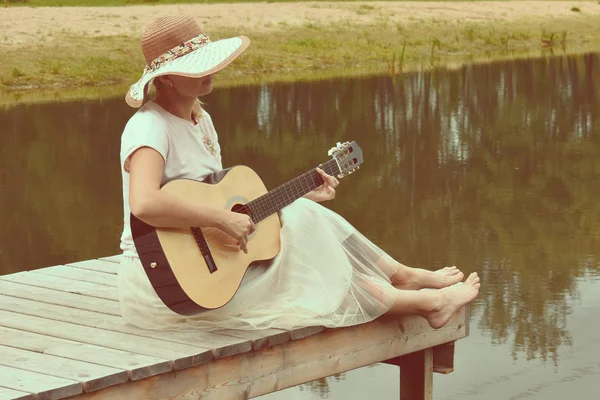 Vrouw in een witte jurk op een Pier met een gitaar. Romantische Moo — Stockfoto