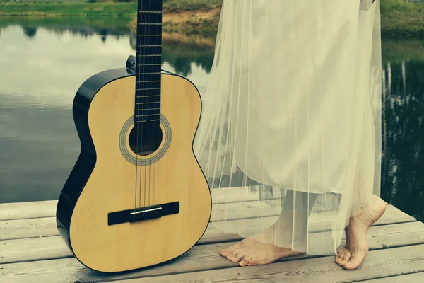 Giovane donna in abito con una chitarra sul lago. Paese picnic outdo — Foto Stock