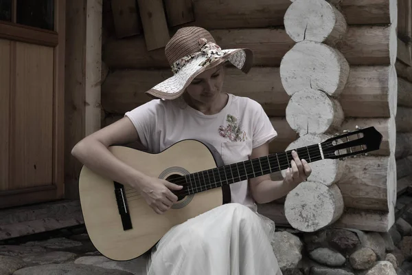 Una ragazza suona la chitarra sotto il portico di una casa di legno . — Foto Stock