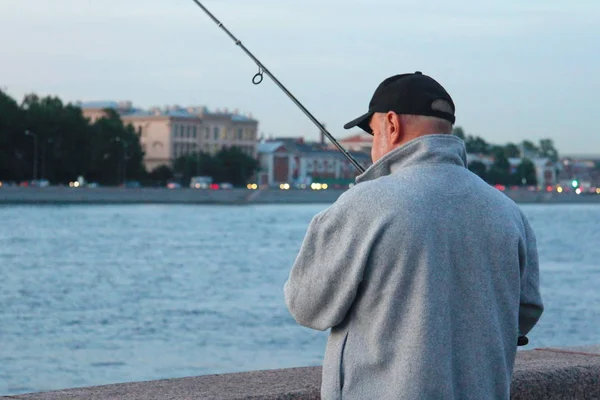 Egy halász horgászik a városi sétányon. Esti horgászat a mellvéden — Stock Fotó