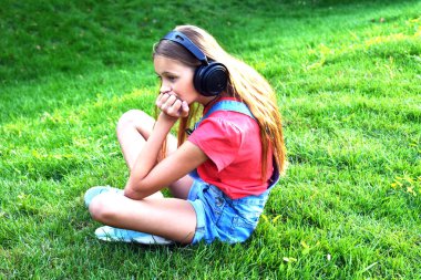 Genç düşünceli bir kız doğada oturur ve kulaklıkla müzik dinler. Gençlik sorunları.