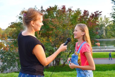 Interviewing girls. Television reporting in the park. clipart