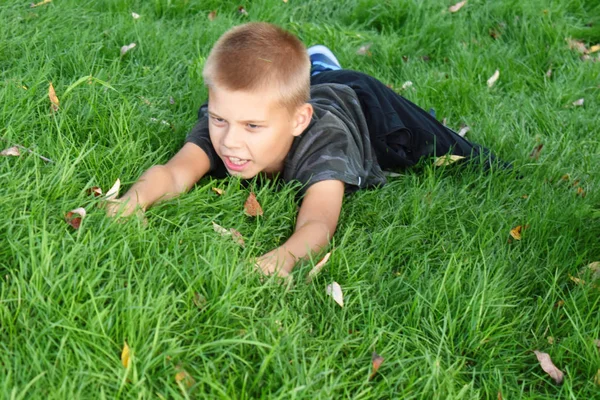 소년은 풀 위로 기어 오릅니다. 풀밭에서 열리는 재미있는 어린이 놀이 — 스톡 사진