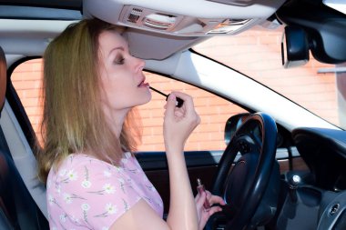 Arabada makyaj yapan bir kadın. Kız dudaklarını rujla boyuyor..