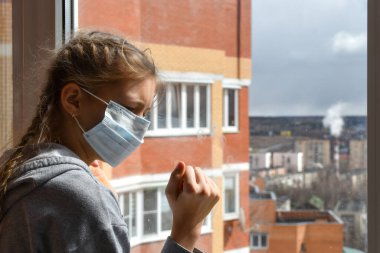 Tıbbi maskeli çocuk pencereden dışarı bakıyor. Dünya salgını