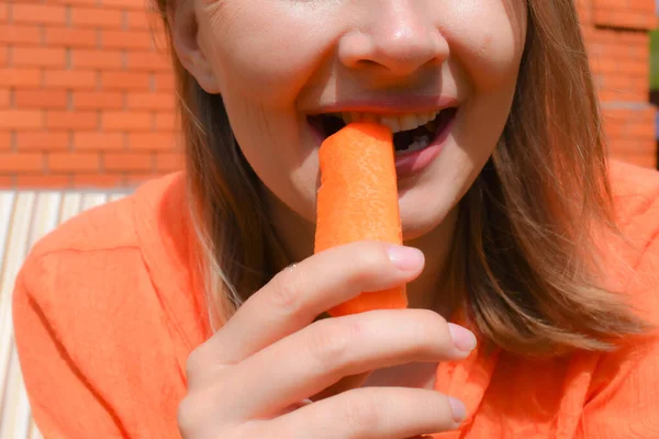 Chica muerde zanahoria cruda al aire libre. Alimento crudo saludable para la salud. Concepto vegetariano —  Fotos de Stock