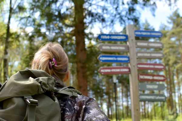 Kobieta patrzy na drewniane drogowskazy w letnim lesie szukając wskazówek. — Zdjęcie stockowe