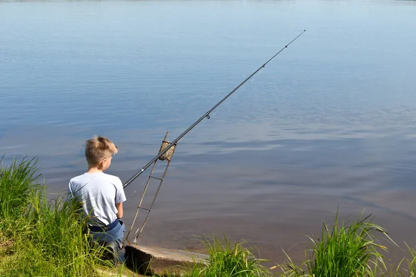 Niño niño pescador se sienta en la orilla y mira flotador. Pesca con niños — Foto de Stock