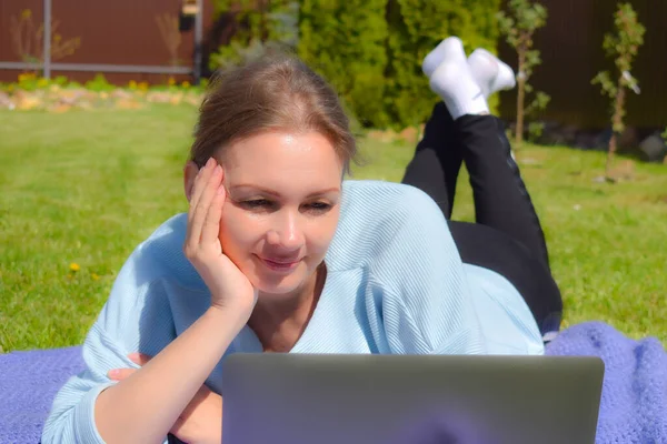 Жінка на траві з ноутбуком дивиться на екран t. Залишайтеся в саду фрілансером — стокове фото