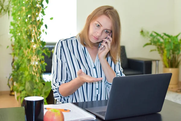 Mulher ansiosa no laptop falando ao telefone em casa — Fotografia de Stock