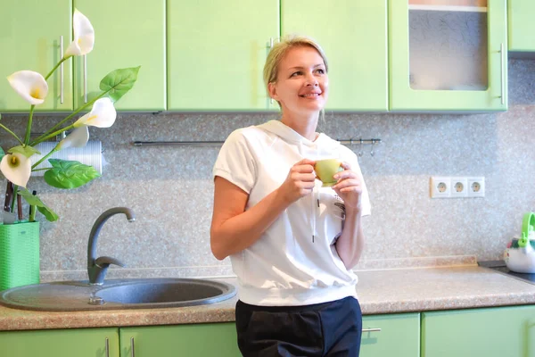 Rire jeune femme avec une tasse de boisson revigorante dans la cuisine à la maison — Photo