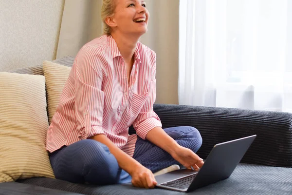 Feliz bela mulher rindo com laptop ri no sofá — Fotografia de Stock