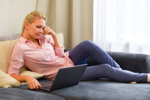 Молода жінка з ноутбуком на дивані дивиться відео курс — стокове фото