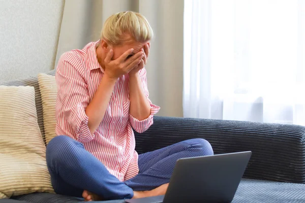 Kvinne med laptop på sofaen dekket ansiktet med hendene. sjokknyheter – stockfoto
