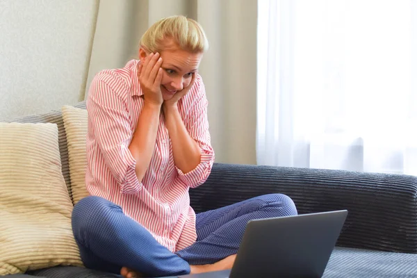 surprised woman with computer on the couch looks at the screen.