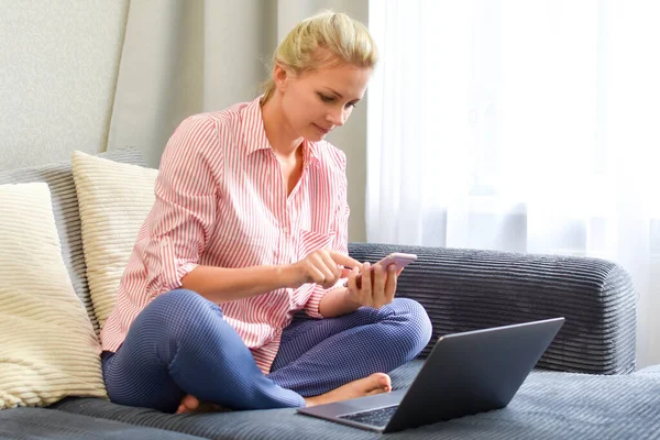 Mulher com um telefone com um computador no sofá faz uma ordem. compras online — Fotografia de Stock