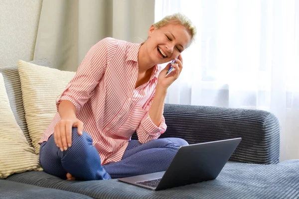 Mulher com telefone rindo alegremente na cama em casa com laptop — Fotografia de Stock