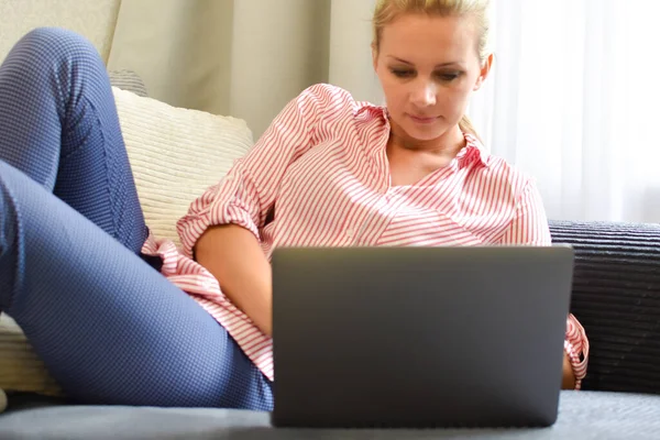 Mulher de 30 anos trabalha em um computador em casa no sofá. um freelancer de sucesso remotamente — Fotografia de Stock