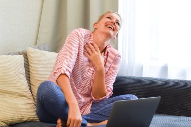 Evdeki bilgisayardaki kanepede gülen sarışın kadın. eğlenceli çevrimiçi iletişim