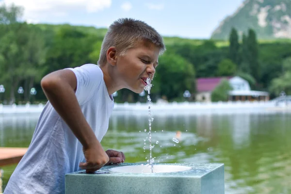 Мальчик пьёт чистую воду из уличного фонтана. Фонтан с родниковой минеральной водой на курорте. — стоковое фото