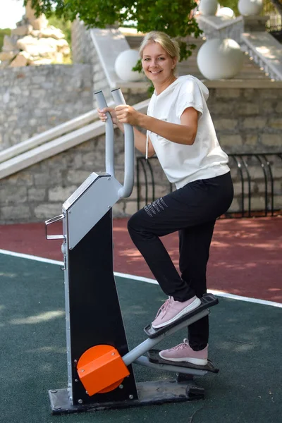 Jonge vrouw traint op de outdoor sport simulator in het park. Gelukkige sportvrouw — Stockfoto