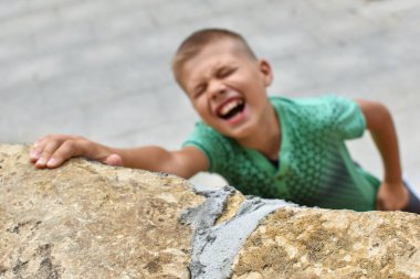risk of falling from mountain. child hangs on wall. dangerous games of children clipart