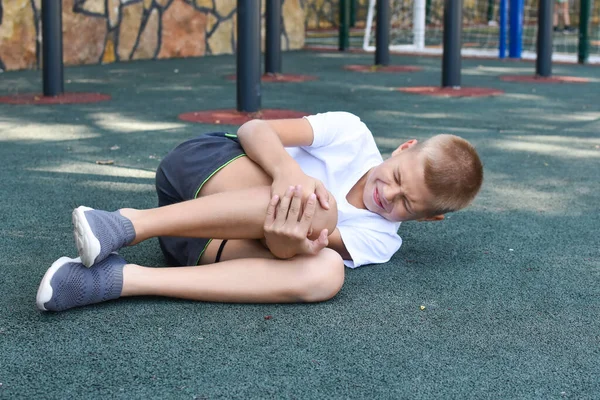 Rapaz caiu e bateu no parque infantil ao ar livre. lesão no joelho lesão esportiva infantil — Fotografia de Stock