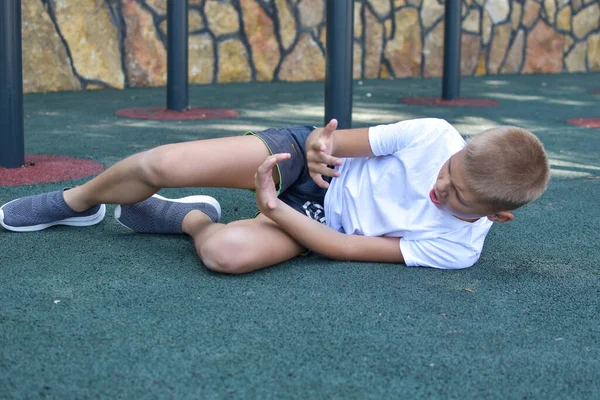 Ребенок спортсмен упал на землю. спортивная травма ноги ребенка. — стоковое фото