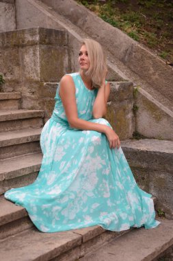 Uzun elbiseli güzel bir kadın taştan bir merdivende oturuyor..