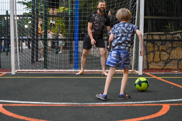Baba ve çocuk açık hava spor sahasında futbol oynuyorlar. Bir ebeveyn küçük bir çocuğu eğitiyor..