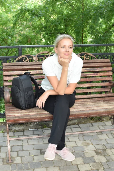 Chica se sienta sola en un banco en un arco en el verano. Mujer esperando a un hombre en una cita — Foto de Stock