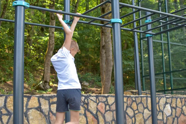 Chico gimnasia al aire libre. Pequeño deportista en la barra horizontal en el parque infantil — Foto de Stock
