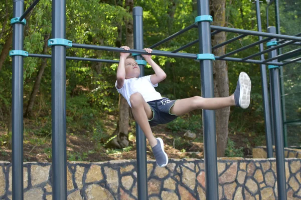 boy gymnastics outdoor. Little sportsman on the horizontal bar on the playground