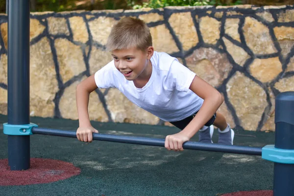 Спортивная гимнастика на открытом воздухе. Маленький спортсмен на горизонтальной полосе на детской площадке — стоковое фото