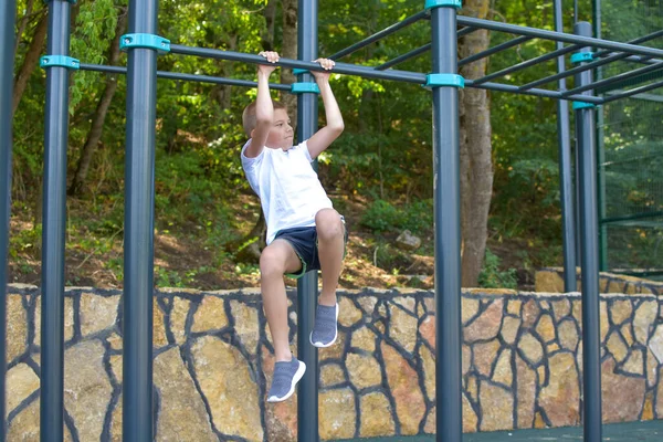 boy gymnastics outdoor. Little sportsman on the horizontal bar on the playground