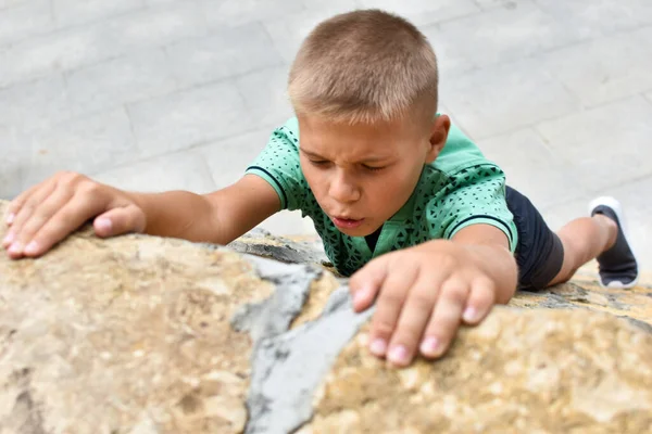 Um menino sobe uma montanha de pedra. persistentemente suba. alcançar o seu objetivo. — Fotografia de Stock