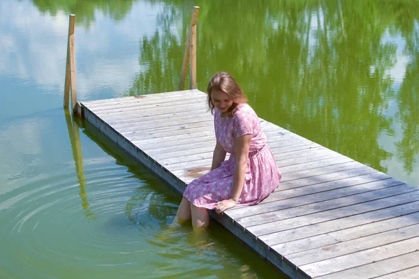 Γυναίκα στη λίμνη στην προβλήτα κάθεται αναπαύεται το καλοκαίρι. — Φωτογραφία Αρχείου