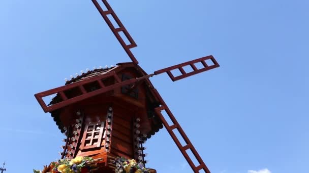 Lindo moinho de madeira decorado com flores e lâmpadas está girando em um fundo azul céu . — Vídeo de Stock