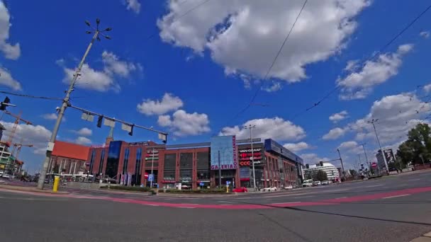 Many cars drive along a city street during rush hour near the shopping center on a background of cloudy blue sky. Time-lapse 4K. — Stock Video