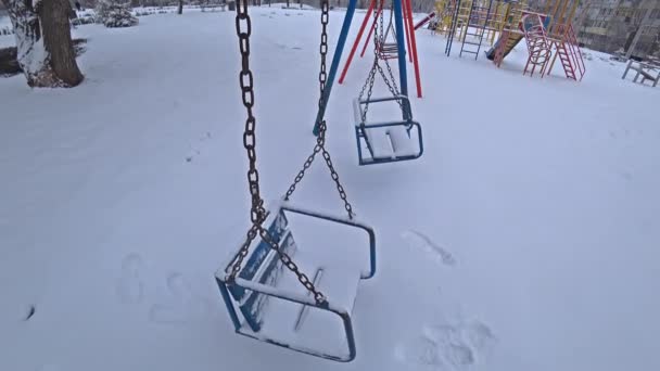 Порожні дитячі гойдалки на дитячому майданчику в міському парку в сонячний зимовий день — стокове відео