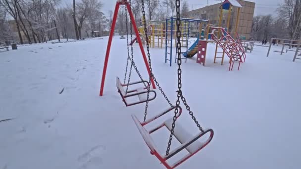 Tom barn svänger på en lekplats i stadsparken på solig vinterdag — Stockvideo
