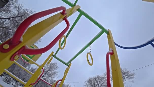 Los niños vacíos se balancean en un parque infantil en el parque de la ciudad en el día de invierno soleado, vista desde abajo, contraluz . — Vídeos de Stock