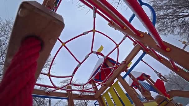 Los niños vacíos se balancean en un parque infantil en el parque de la ciudad en el día de invierno soleado, vista desde abajo, contraluz . — Vídeo de stock