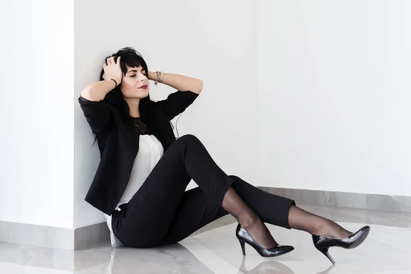 Hermosa mujer joven cansada vestida con un traje de negocios negro sentarse — Foto de Stock