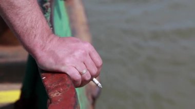 Erkek el sigara bir tekne yakın yukarı bir sigara. Arka planda bir nehir AF.