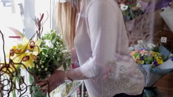 女孩花店安排鲜花 并选择三个美丽的新鲜黄色兰花在花店的窗口附近花束 — 图库视频影像